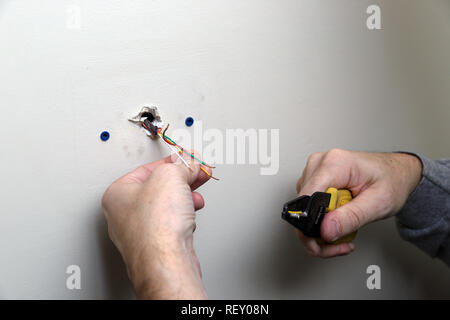 Close-up of hand holding Control wire for thermostat used with a HVAC unit, coming out of wall during installation Stock Photo