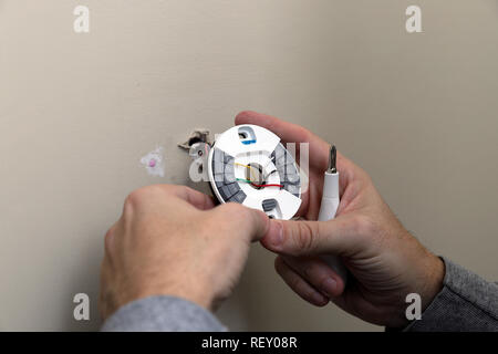 Close-up of Hand installing wires and mounting plate for modern round thermostat for air conditioning unit in a house Stock Photo