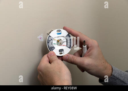 Close-up of Hand installing wires and mounting plate for modern round thermostat for air conditioning unit in a house Stock Photo