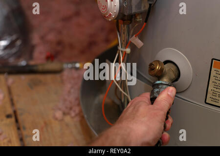 Hand attaches hose to water heater drain to perform maintenance Stock Photo