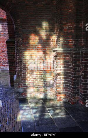 Sunlight shines through an arched window, casting interesting shapes on an old brick wall, Amsterdam, Europe. Stock Photo