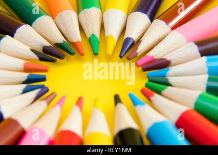 An assortment of colour pencils in circle, spiral on yellow background. School supplies, creativity concept Stock Photo