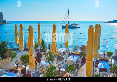 ST JULIANS, MALTA - JUNE 20, 2018: The picturesque seascape from the coast of the city with the nice outdoor restaurant on the foreground, on June 20  Stock Photo