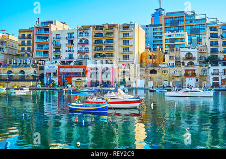 ST JULIANS, MALTA - JUNE 20, 2018: The colorful boats are moored in Spinola Bay harbour, surrounded by modern residential quarters, stores and tourist Stock Photo