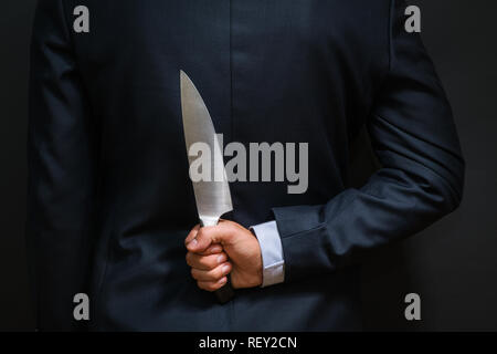 Criminal with big knife hidden behind his back. Cold weapon, burglary Stock Photo