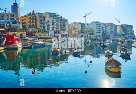 ST JULIANS, MALTA - JUNE 20, 2018: Spinola Bay is full of small fishing boats and yachts, it's surrounded by coastal cafes, hotels and souvenir stores Stock Photo