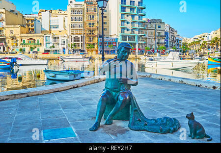 ST JULIANS, MALTA - JUNE 20, 2018: Maltese fisherman statue with net and cat, asking for the fish, stands at Spinola Bay with numerous fishing boats o Stock Photo