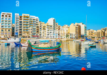 ST JULIANS, MALTA - JUNE 20, 2018: The line of modern residential buildings behind the Spinola Bay with many fishing boat, bobbing on the gentle waves Stock Photo
