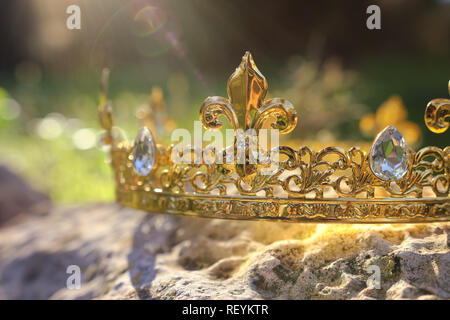 mysterious and magical photo of gold king crown over the stone in the England woods or field landscape with light flare. Medieval period concept Stock Photo