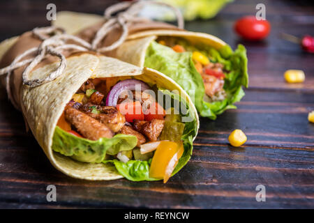 Traditional mexican tortilla wrap with vegetables and grilled chicken meat on dark wood table Stock Photo