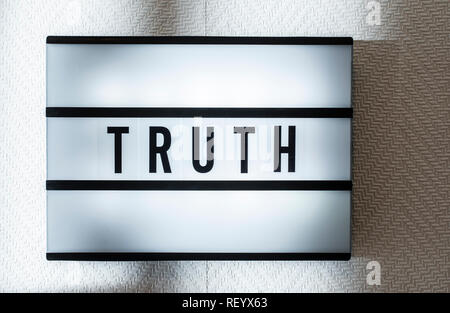 Message Truth on illuminated board. Truthfulness concept with text. Daylight from window. Room interior. Black letters Truth on white wallpaper wall. Stock Photo