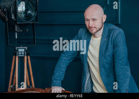 Portrait of attractive adult successful bald bearded man in suit on blue background, blogging, TV host