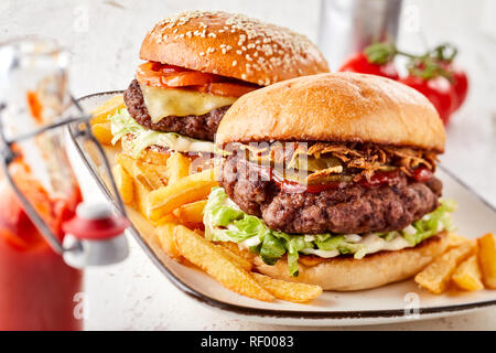 Two assorted burgers on crusty toasted buns with all the trimmings served with French fries and ketchup on a rectangular platter Stock Photo