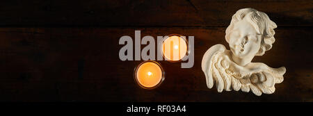 Panoramic banner with angel and burning candles over a dark background with copy space for concepts of bereavement, sorrow and mourning Stock Photo