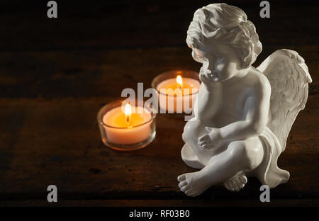 Angel figurine with burning candles on a dark wood background with copy space conceptual of sorrow and bereavement Stock Photo