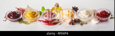 Panorama banner of assorted sauces, dressings and marinades with spices, herbs, oil, onion and fresh garlic high angle on white Stock Photo