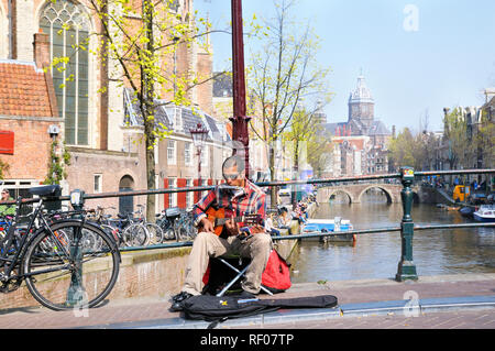 Busker playing guitar and harmonica on a warm spring day in the Red Light District, Amsterdam, North Holland, Netherlands Stock Photo