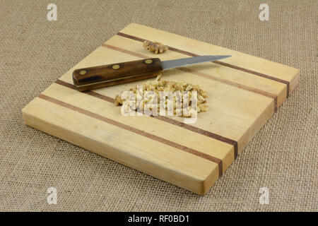 Minced walnut nuts on wooden cutting board with kitchen knife Stock Photo