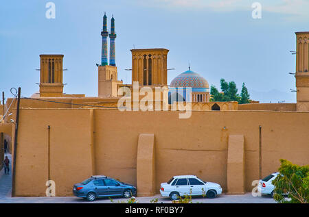 The tall minarets and bright blue dome of Jameh Mosque behind the huge adobe walls and badgirs (wind towers) of historic mansion in Fahadan district,  Stock Photo