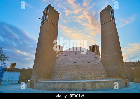 The evening walk in old Yazd with a view on yakhchal (ice chamber) with tall wind towers (badgirs) and bright sunset sky on the background, Iran. Stock Photo