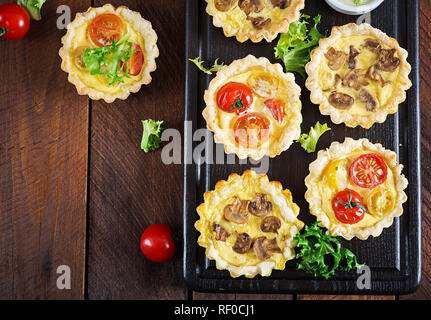 Mushrooms, cheddar, tomatoes tartlets on wooden background. Mini pies. Delicious appetizer, tapas, snack. Top view. Flat lay Stock Photo