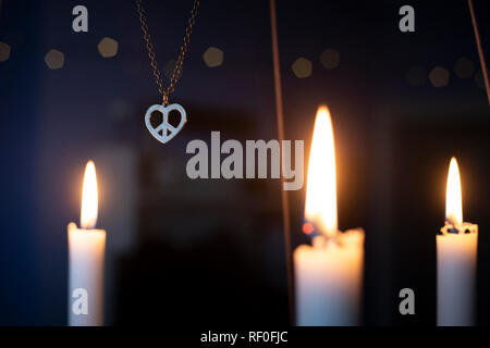 Peace, love, christmas  background with a peace heart symbol pendant hanging among candles glowing on a golden advent chandelier. Stock Photo