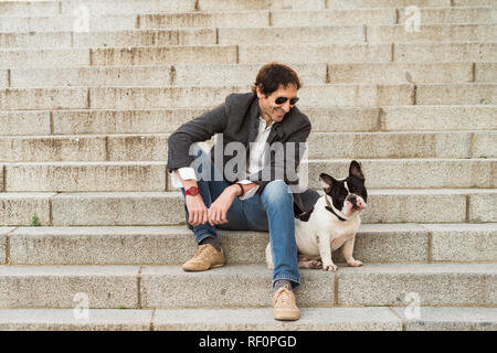 Urban scene. Man dressed in casual clothes sitting on some stairs posing next to his dog Stock Photo