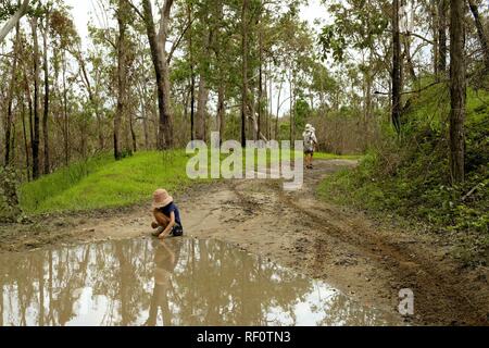 A child plays in a muddy puddle along a four wheel drive track through a forest, Mia Mia State Forest, Queensland, Australia Stock Photo