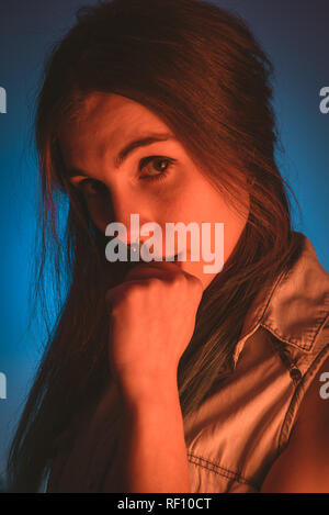 Charming young lady with piercing and fist near mouth looking at camera in redness on blue background Stock Photo