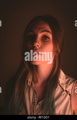 Charming young lady with piercing looking at camera in brown background Stock Photo
