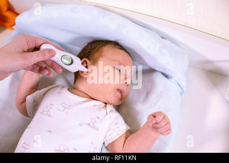 Measuring baby's temperature with contactless thermometer. Mom measures the baby's body temperature with a thermometer in the ear Stock Photo