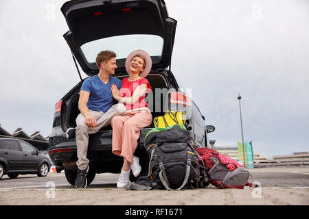 Happy young couple sitting in car boot at the airport Stock Photo