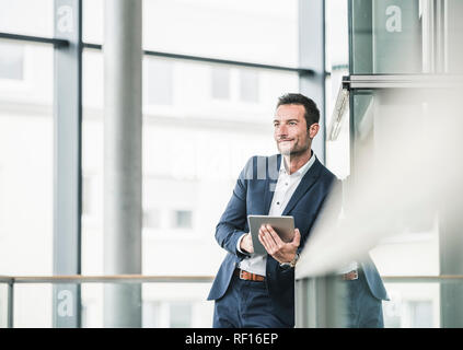 Businessman standing in office building, using digital tablet Stock Photo