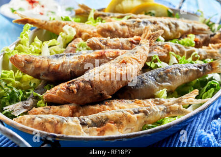 Traditional Greek crispy fried sardines in batter on a bed of fresh green lettuce in a close up view Stock Photo