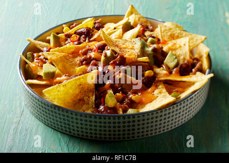 Spicy chili con carne with Mexican nachos, melted cheese and avocado baked in the oven viewed close up high angle over green wood Stock Photo