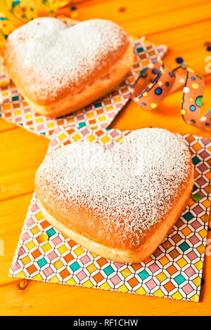 Two heart shaped freshly baked romantic cakes displayed on pretty paper with a colorful geometric pattern on yellow wood Stock Photo