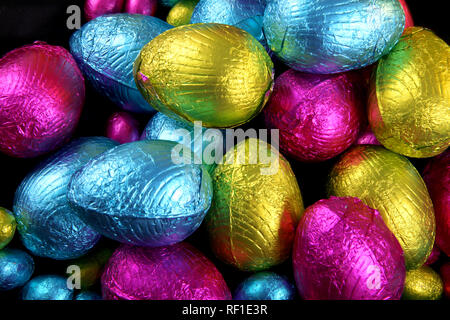 Pile of foil wrapped chocolate easter eggs in pink, blue & lime green. Stock Photo