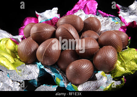 Pile of unwrapped chocolate easter eggs with the colorful foil wrapping surrounding it on a black background. Stock Photo