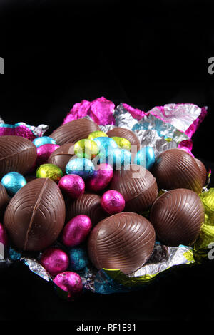 Pile of unwrapped chocolate easter eggs with the colorful foil wrapping surrounding it on a black background. Stock Photo