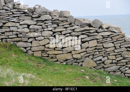 Dry stone wall on the Isle of Purbeck, Dorset. Rough limestone wall divides sloping coastal fields with the sea in the background. Stock Photo