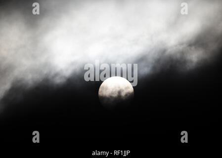 Bright disc of a winter sun behind heavy clouds. Stormy and harsh. Colourless. Colorless Stock Photo