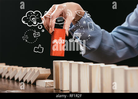 cropped view of woman picking red block with word 'audit' out of wooden bricks, icons on foreground Stock Photo