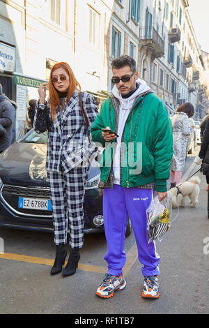MILAN, ITALY - JANUARY 13, 2019: Woman with black and white checkered suit and man with green bomber jacket looking at smartphone before John Richmond Stock Photo