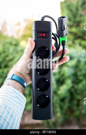 Man holding against green background power strip with four power outlets and IEC power cord to be used in back-up ups Stock Photo