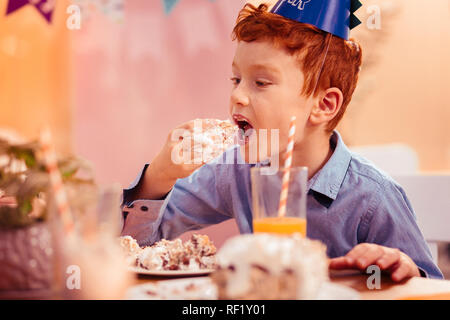 Hungry red-haired boy eating tasty birthday cake Stock Photo