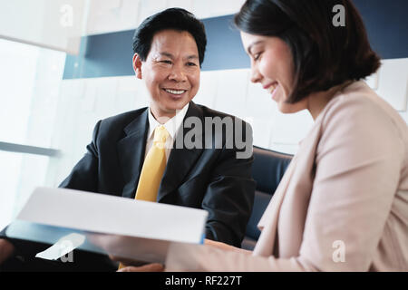 Investment Plan Agent Showing Documents To Asian Customer In Bank Stock Photo