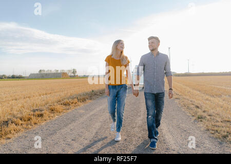 Young couple walking on dirt track at camper van in rural landscape Stock Photo
