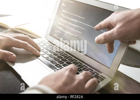 person working on laptop computer while other is pointing at monitor Stock Photo