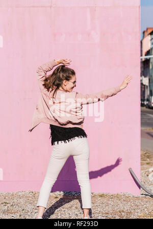 Happy young woman moving in front of pink wall Stock Photo - Alamy