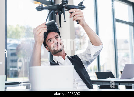 Businessman sitting in office working on a drone, using VR glasses Stock Photo